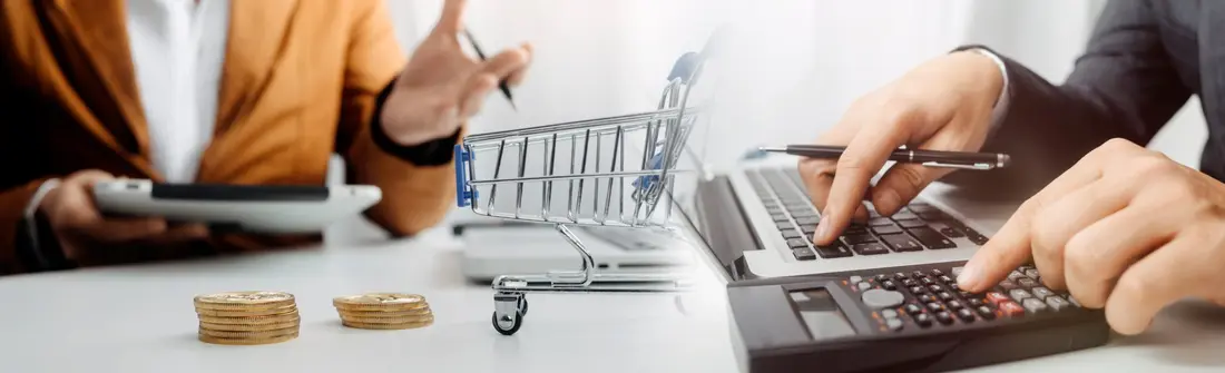 Coins, a small shopping trolley and a calculator on a desk
