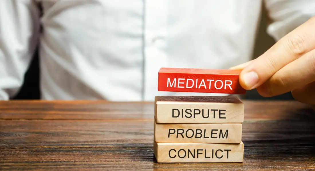 Hand placing a mediator block on blocks marked dispute, problem and conflict
