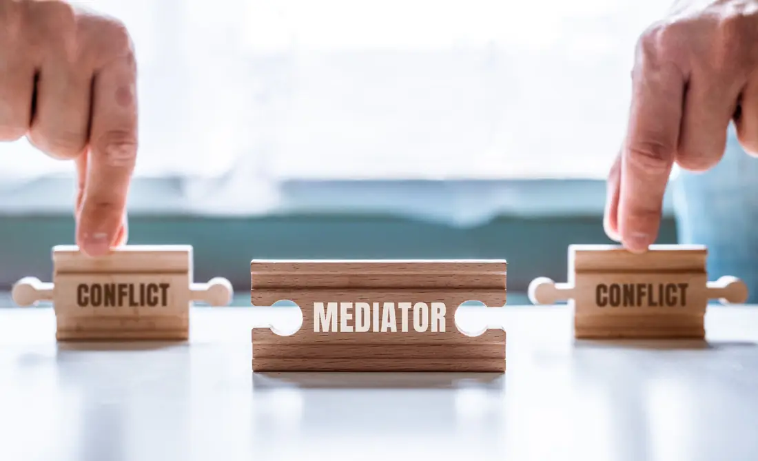 Wooden puzzle pieces marked conflict joined by a piece marked mediator