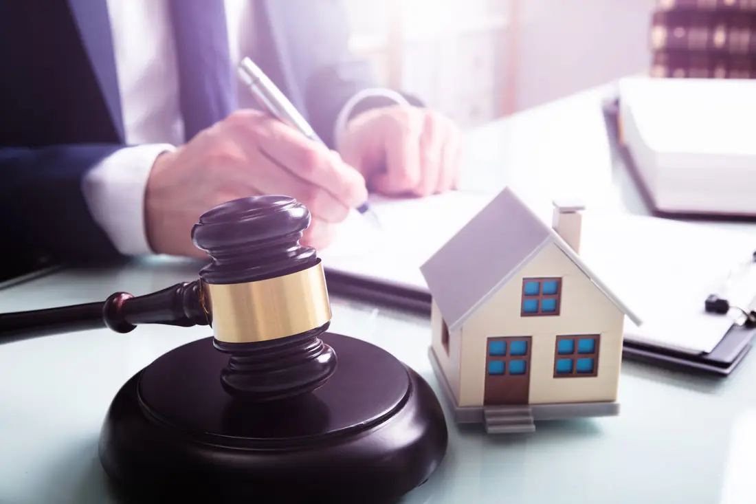 Solicitor signing documents beside a gavel and a model house