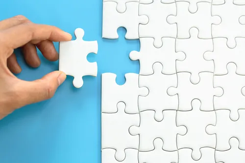 Hand placing the last piece of a white puzzle